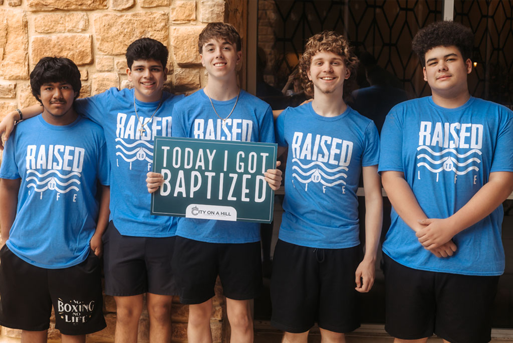 Two people standing in a pool of water wearing blue shirts that say raised to life.
